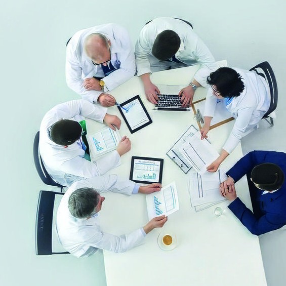 Team di professionisti riuniti attorno a un tavolo, ripresi dall'alto, con tablet e documenti di analisi.